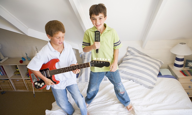 Two Boys Standing On A Bed, Playing Guitar And Singing Into A Hairbrush
