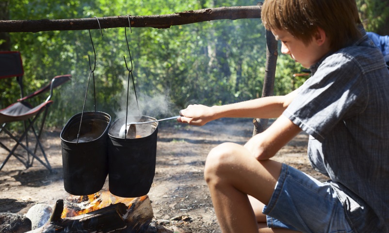 Young boy cooking camp food in cauldron on open fire